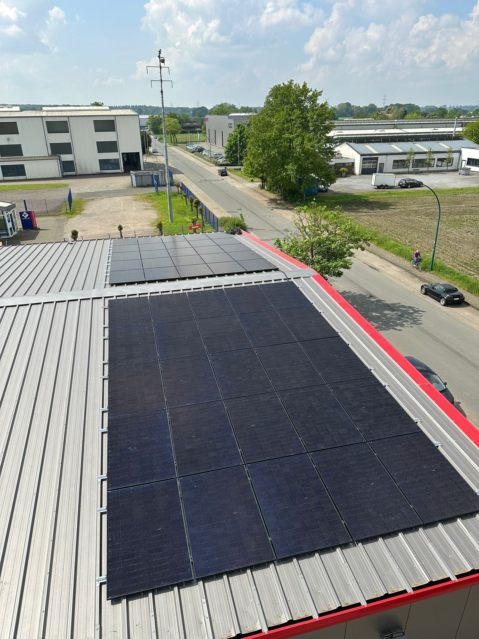 Solarmodule auf einem Dach, im Hintergrund sind eine Straße, Gebäude und ein Baum zu sehen.