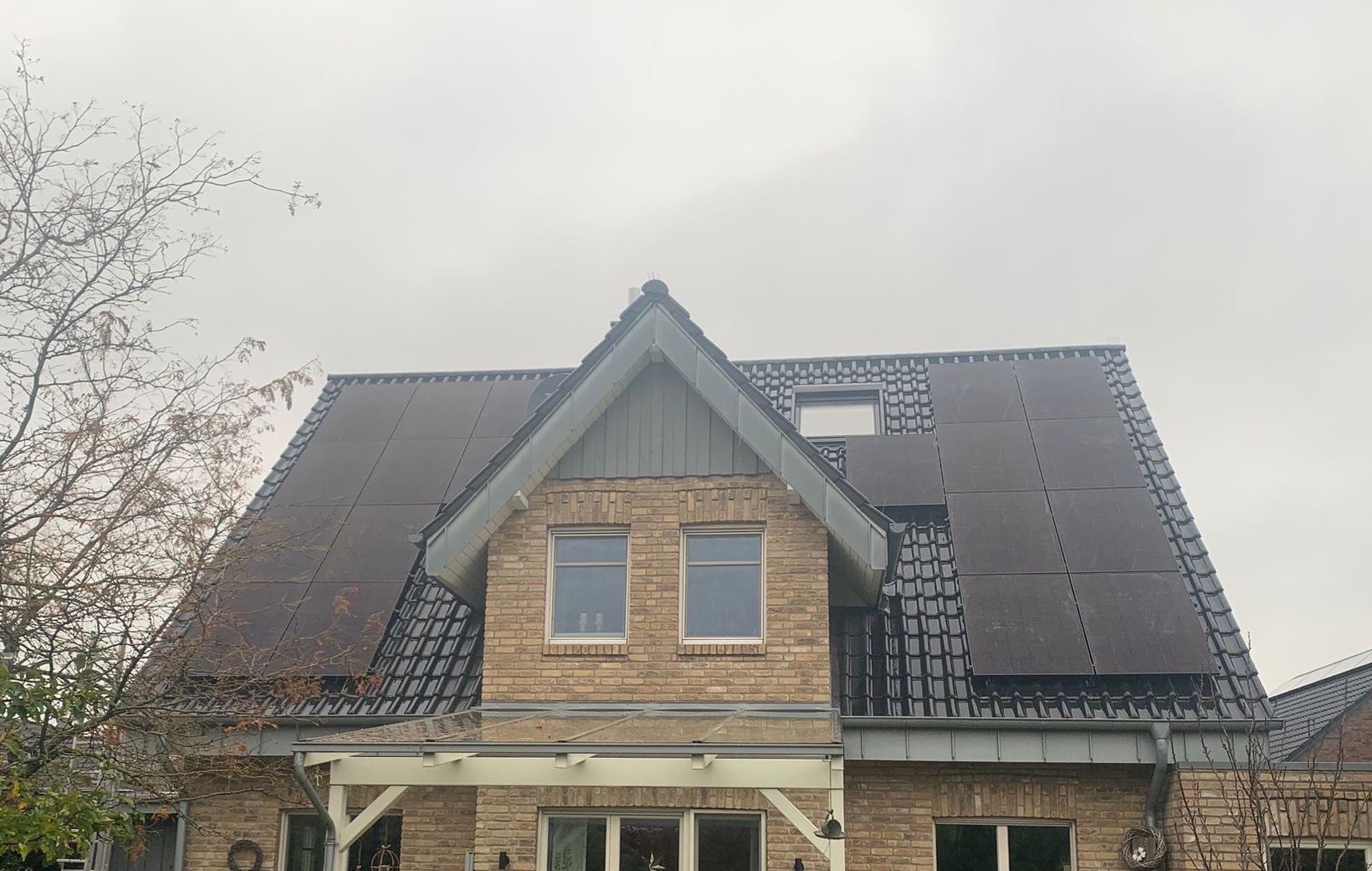 Haus mit Ziegelfassade und Solarzellen auf dem Dach vor bewölktem Himmel.