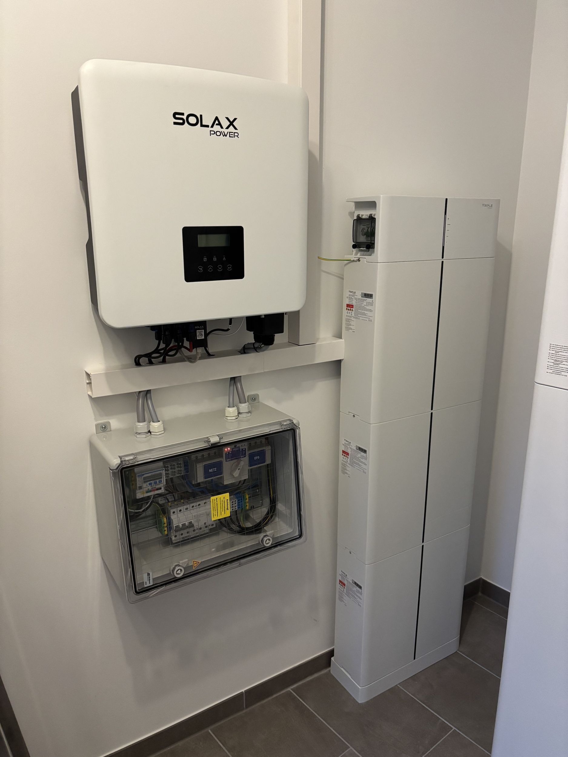 Weißer Solarwechselrichter, Schaltkasten und Batteriesystem an einer Wand montiert.