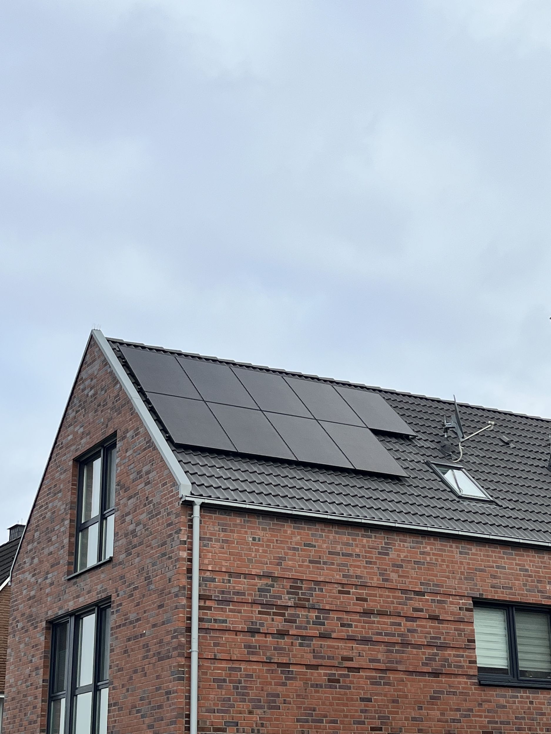 Rotes Backsteinhaus mit Sonnenkollektoren auf einem grauen Ziegeldach unter einem bewölkten Himmel.