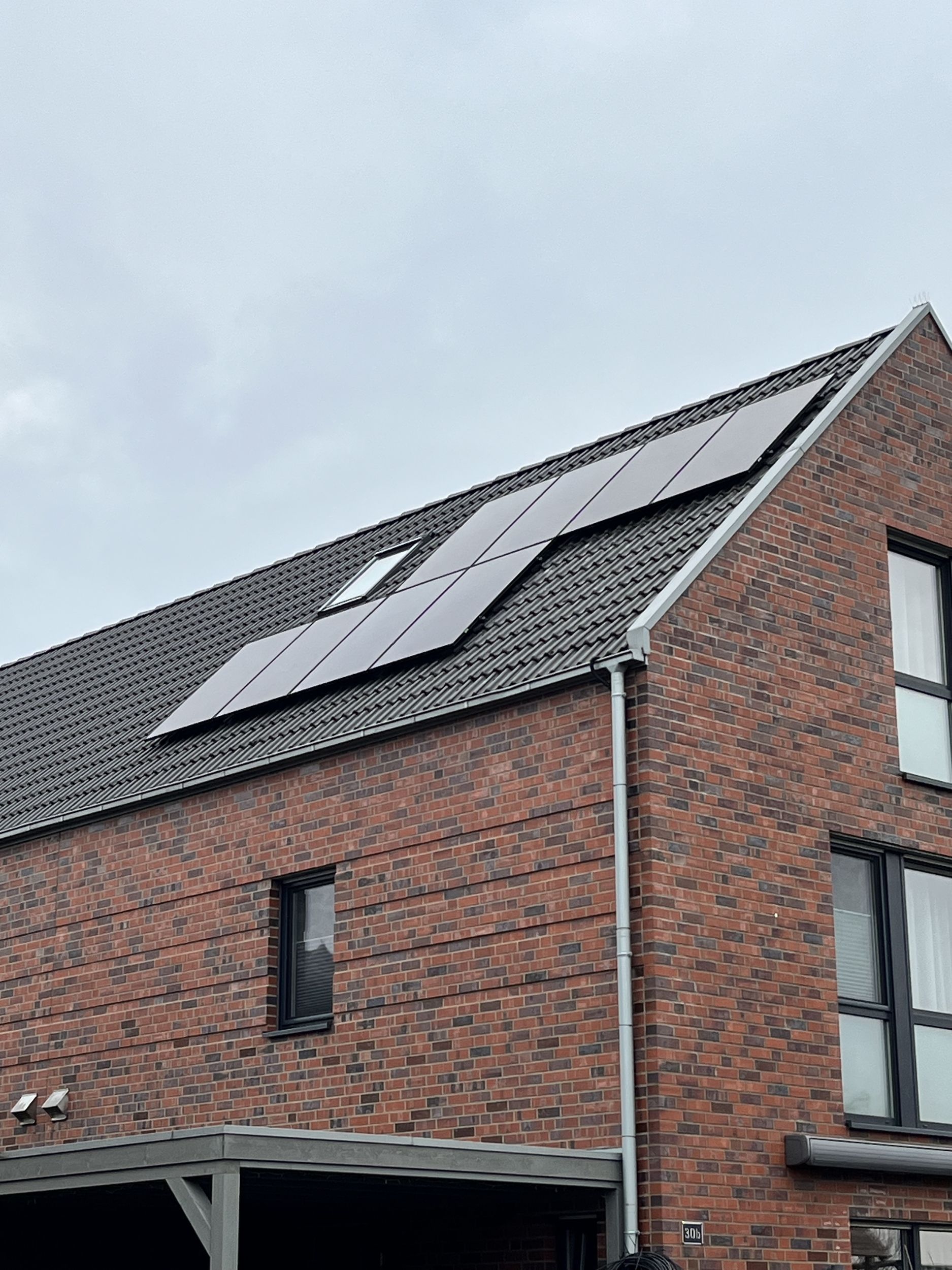 Rotes Backsteinhaus mit Sonnenkollektoren auf dem Dach unter bewölktem Himmel.
