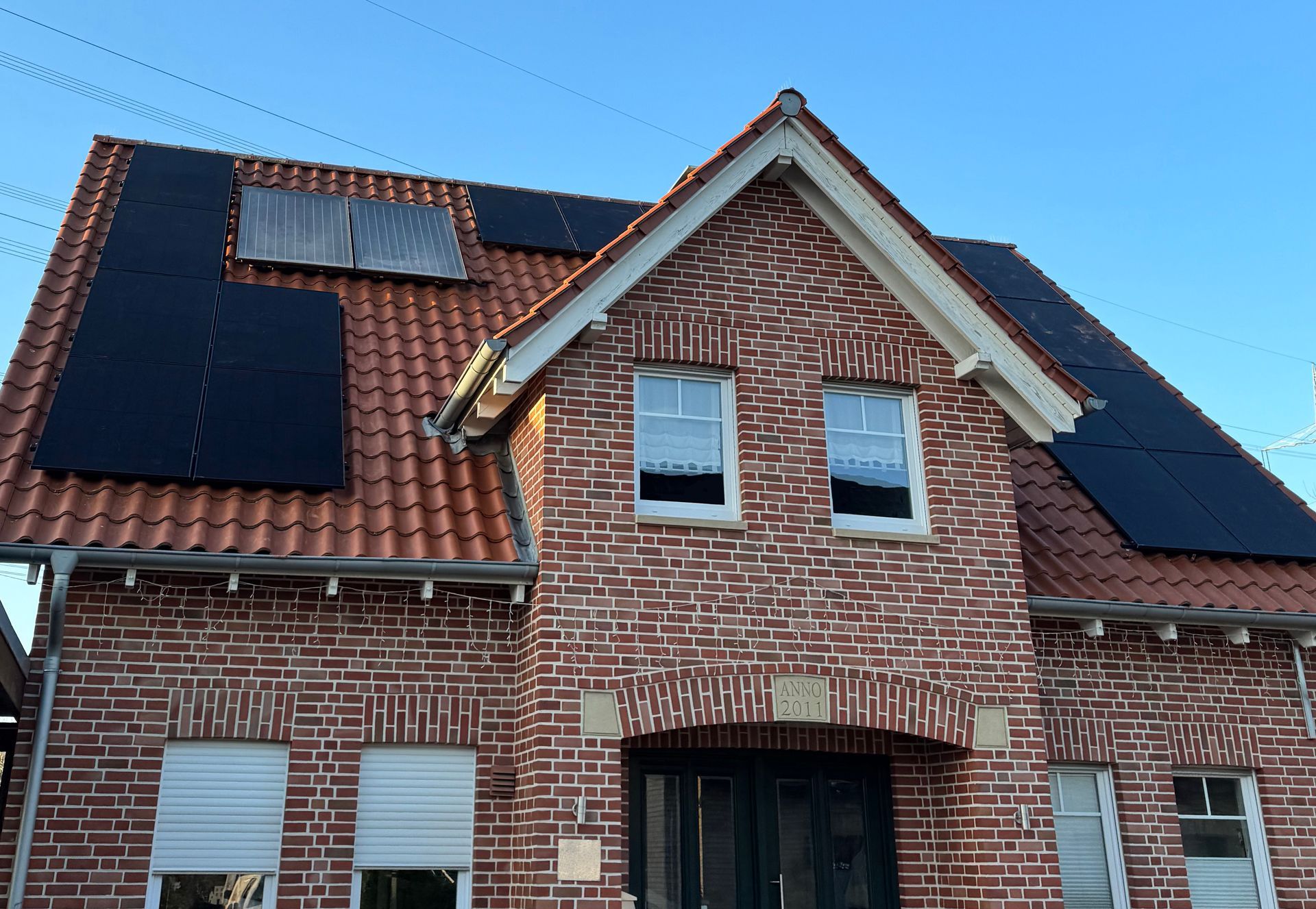 Backsteinhaus mit rotem Ziegeldach, Solarmodulen und zwei Fenstern im oberen Stockwerk.