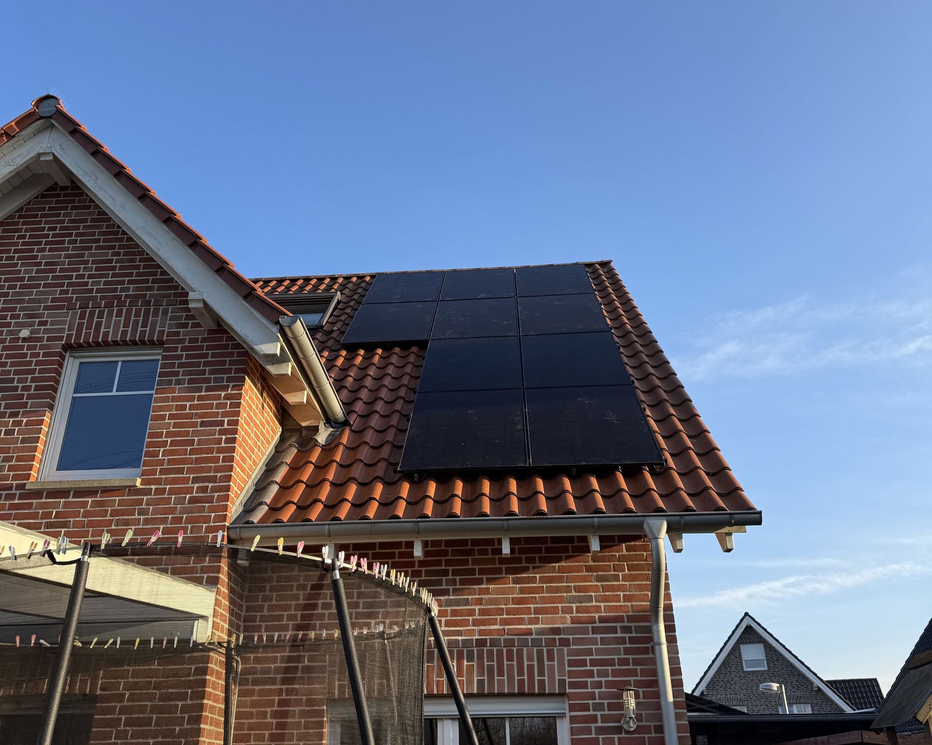 Backsteinhaus mit Solarzellen auf dem Dach unter einem klaren blauen Himmel.
