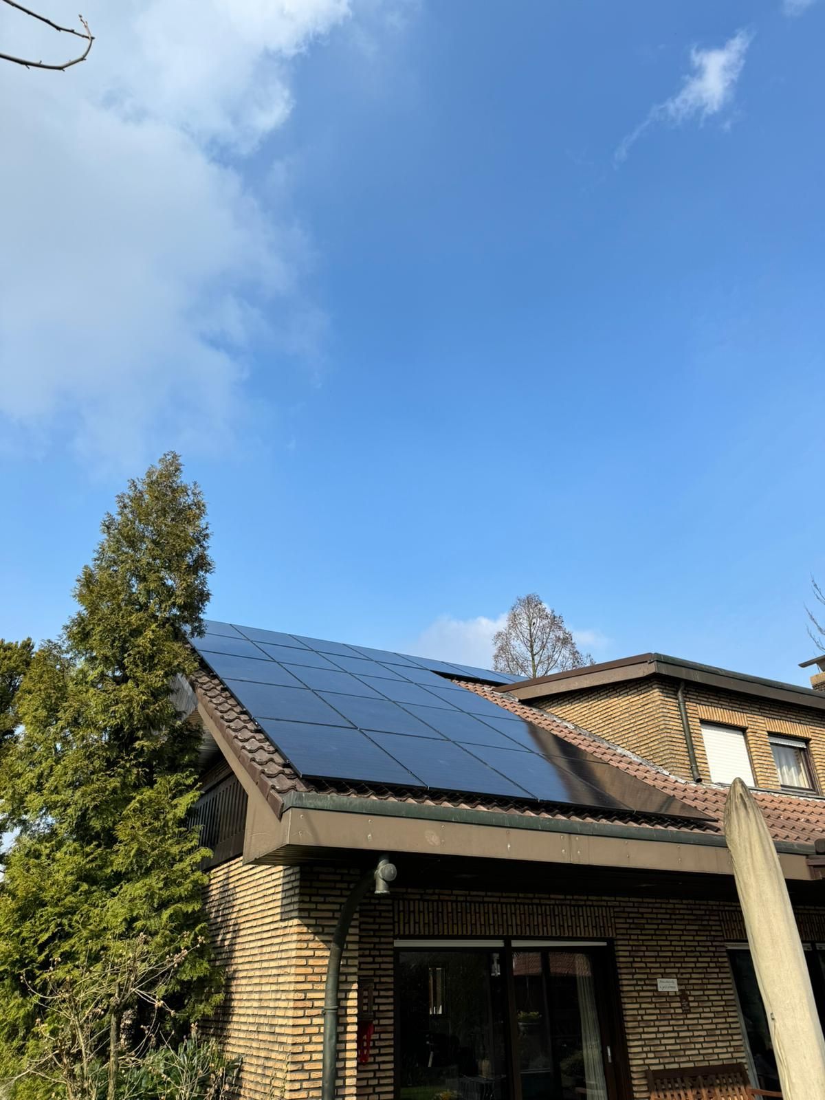 Solarmodule auf einem braunen Backsteinhausdach unter einem blauen Himmel mit ein paar Wolken.