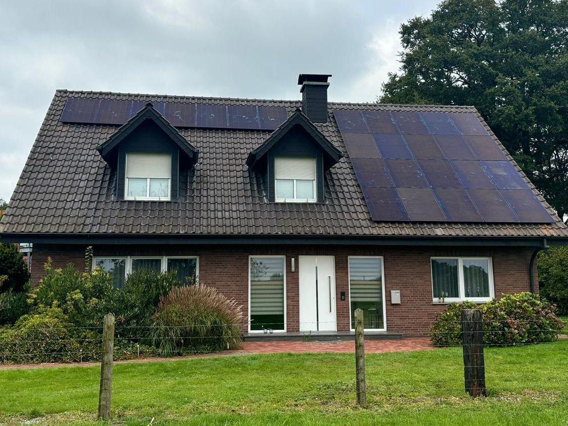 Backsteinhaus mit Solarzellen auf dem Dach und einem grünen Rasen im Vordergrund.