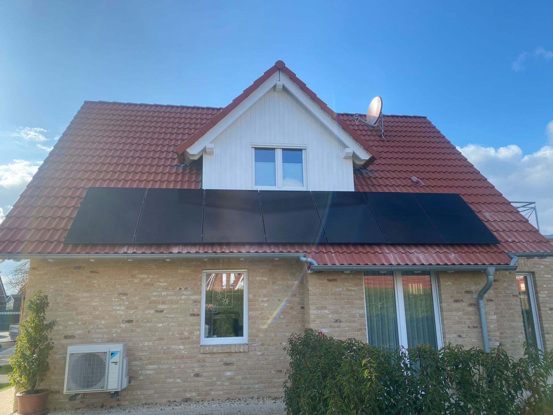 Unter einem klaren blauen Himmel sind auf dem roten Ziegeldach eines Backsteinhauses Solarmodule installiert.