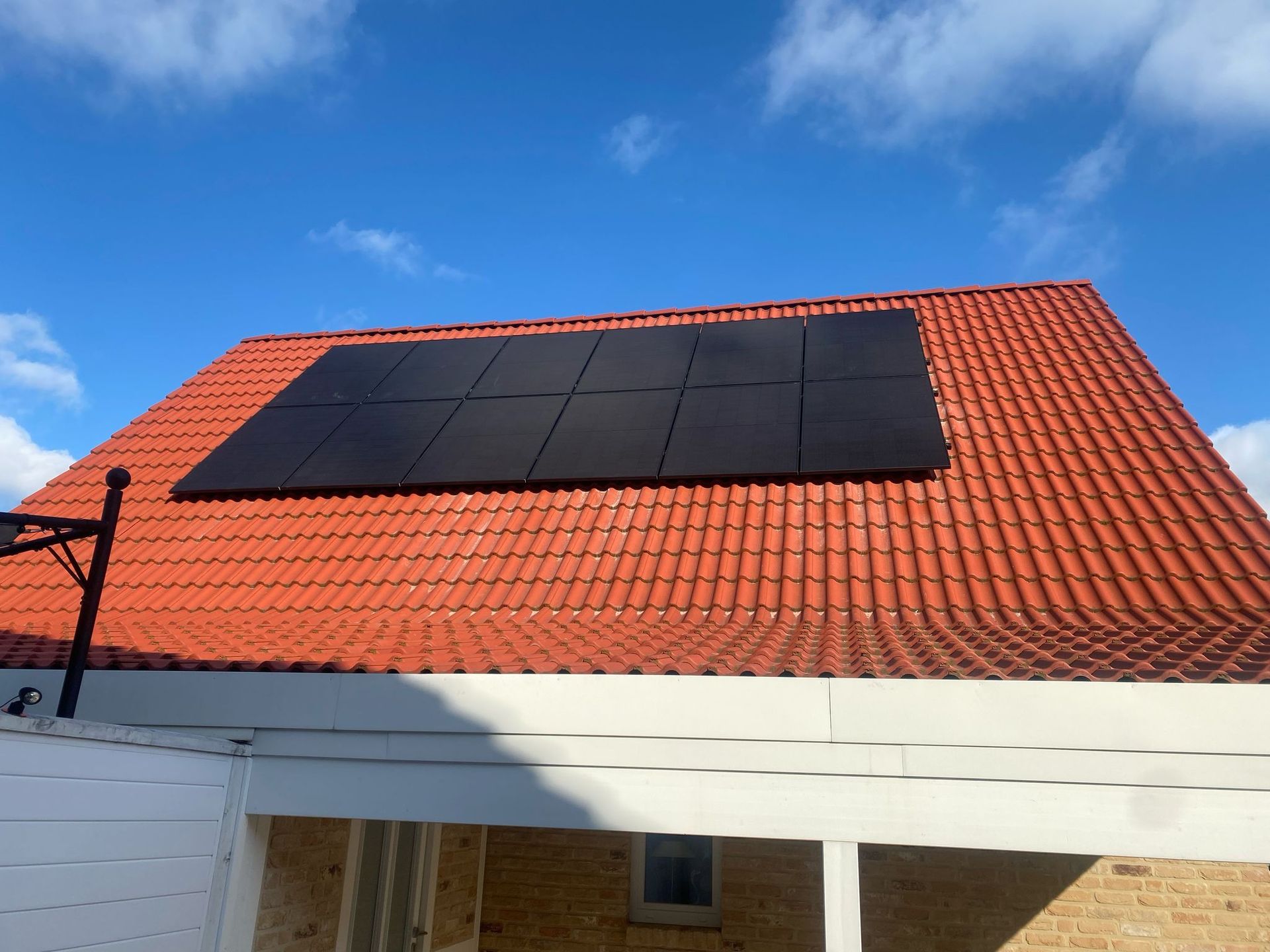 Solarmodule auf einem roten Ziegeldach vor einem blauen Himmel mit vereinzelten Wolken.