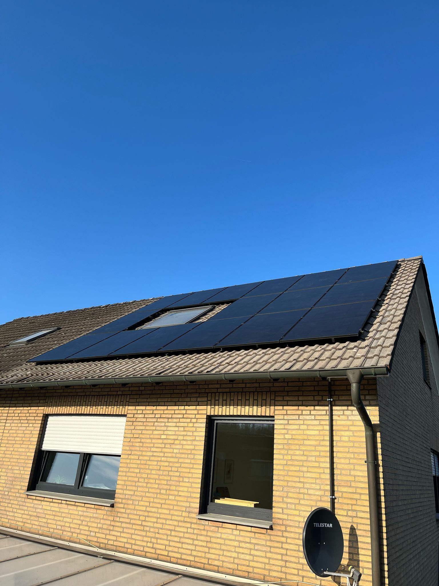 Solarmodule auf dem Dach eines Backsteinhauses vor einem klaren blauen Himmel.