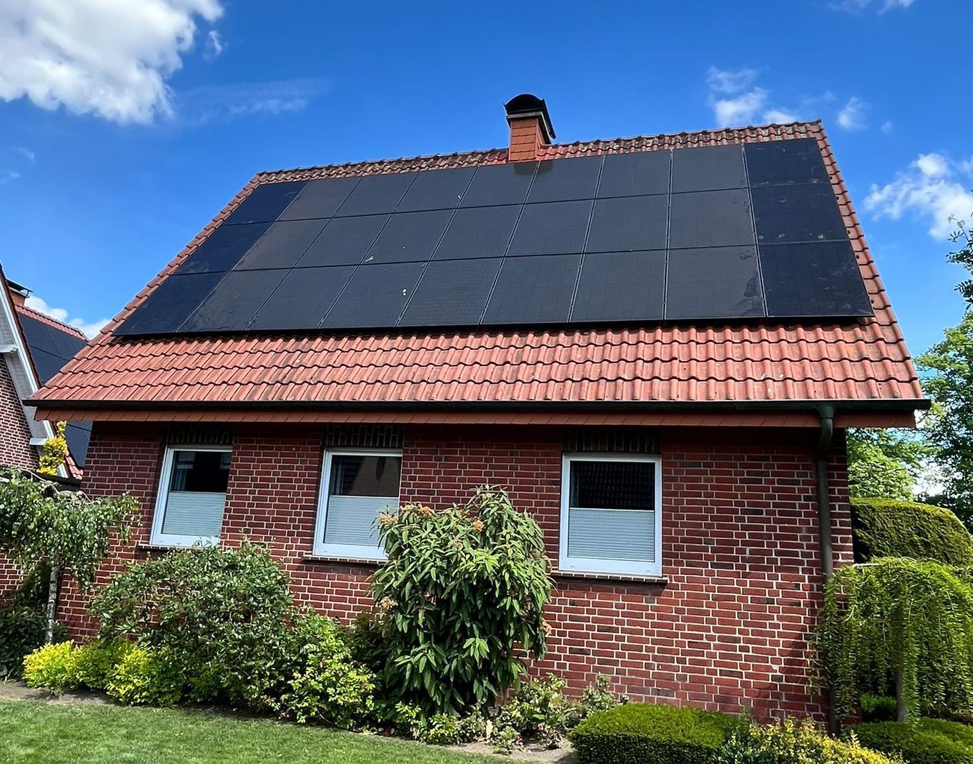 Backsteinhaus mit Solarzellen auf einem Ziegeldach unter blauem Himmel.