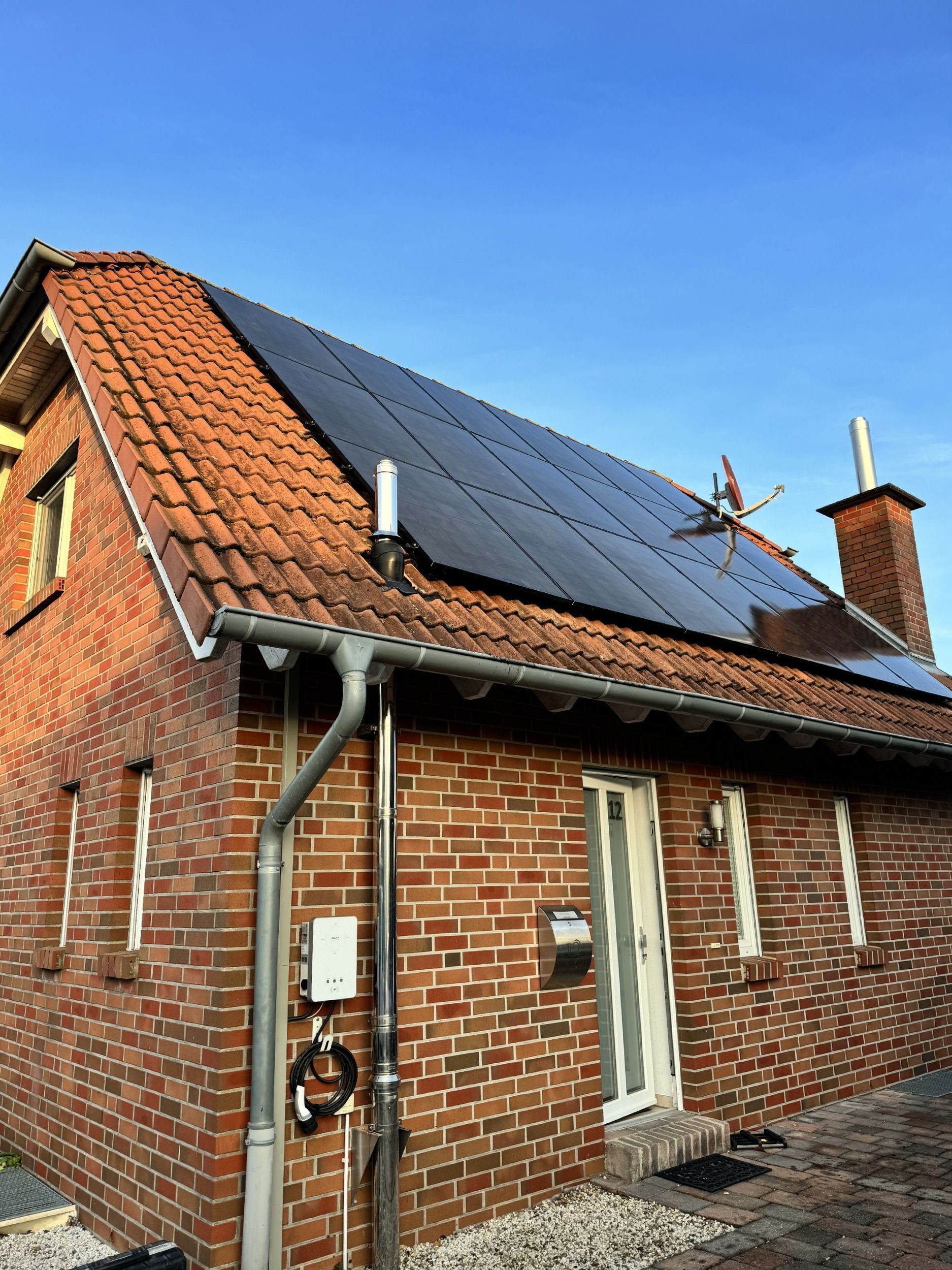 Rotes Backsteinhaus mit Solarzellen auf dem Dach, darüber ein klarer blauer Himmel.