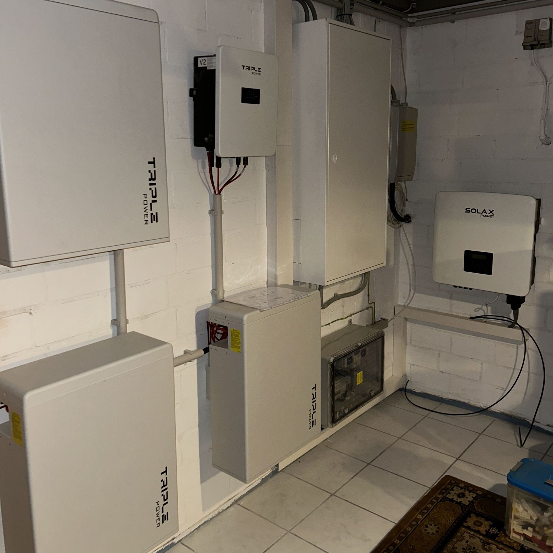 In einem Keller installierte Solaranlage. Weiße Einheiten säumen die Wand zusammen mit schwarzen Bedienfeldern.