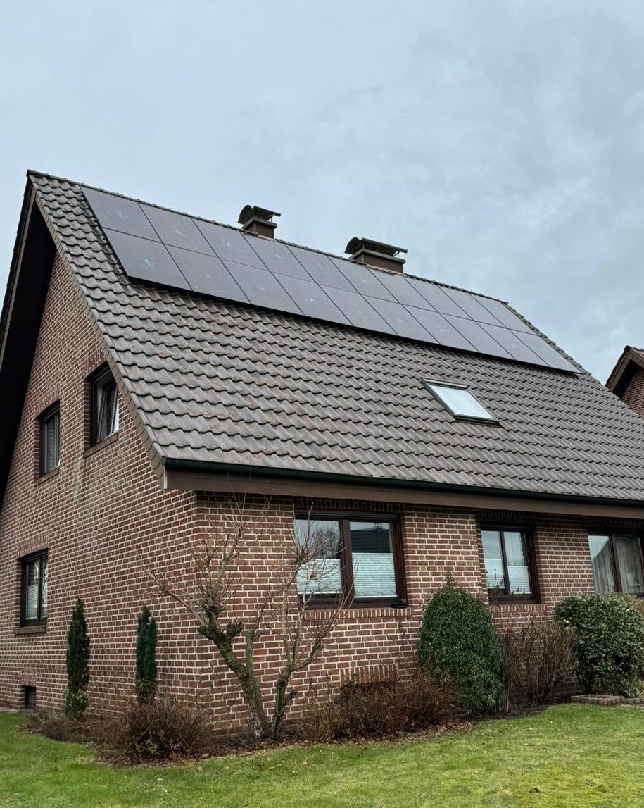 Backsteinhaus mit Sonnenkollektoren auf dem Dach unter bewölktem Himmel.