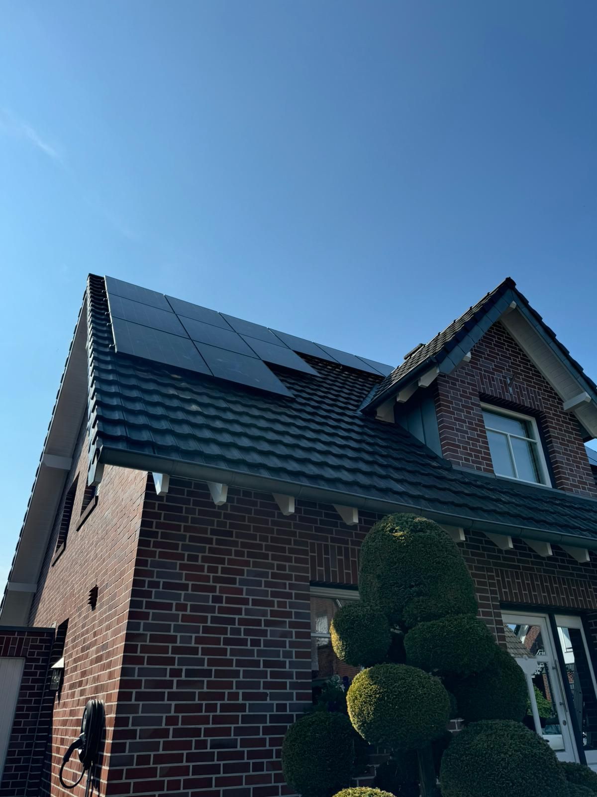Backsteinhaus mit Solarzellen auf dem Dach vor einem klaren blauen Himmel.