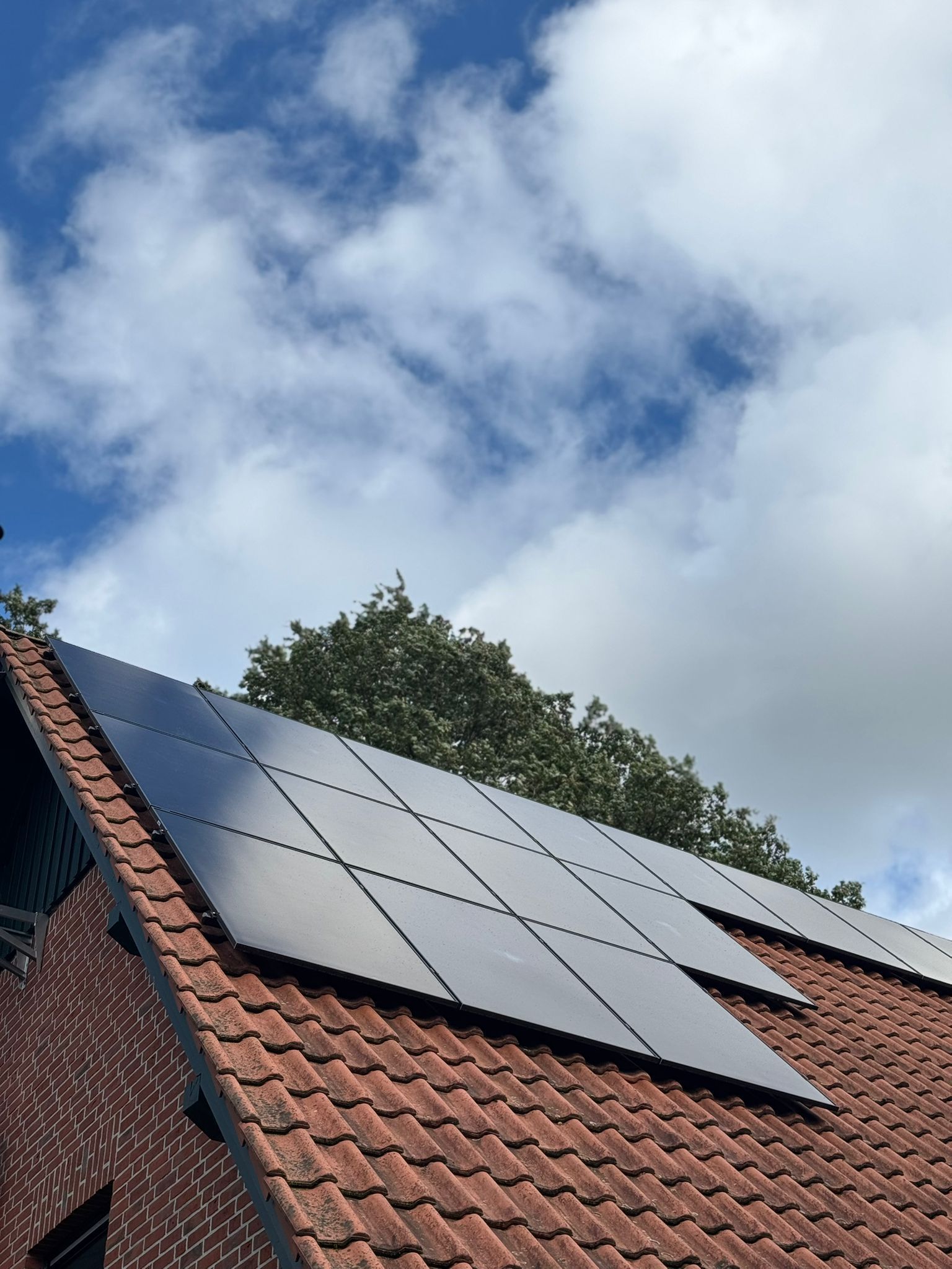 Solarmodule auf einem roten Ziegeldach vor einem bewölkten blauen Himmel.
