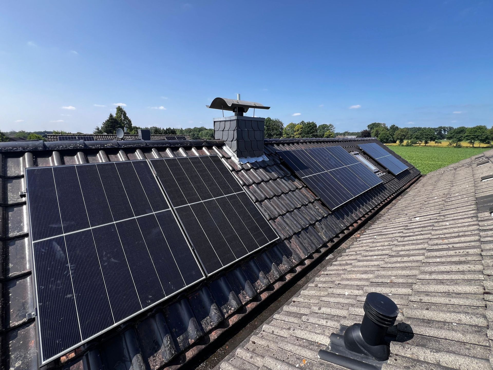 Solarmodule auf einem Ziegeldach mit Schornstein unter blauem Himmel.