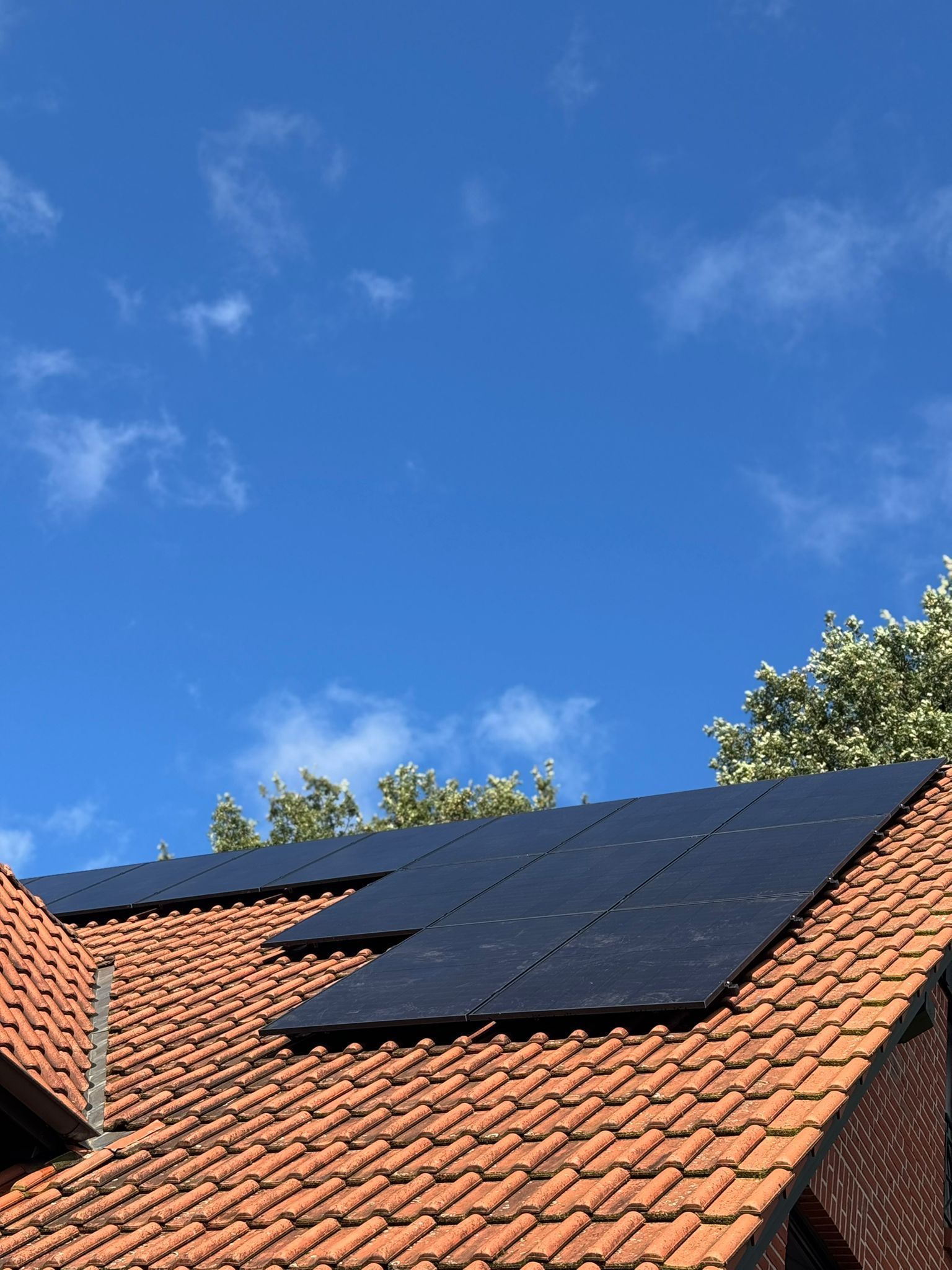 Solarmodule auf einem roten Ziegeldach vor einem strahlend blauen Himmel mit dünnen Wolken.