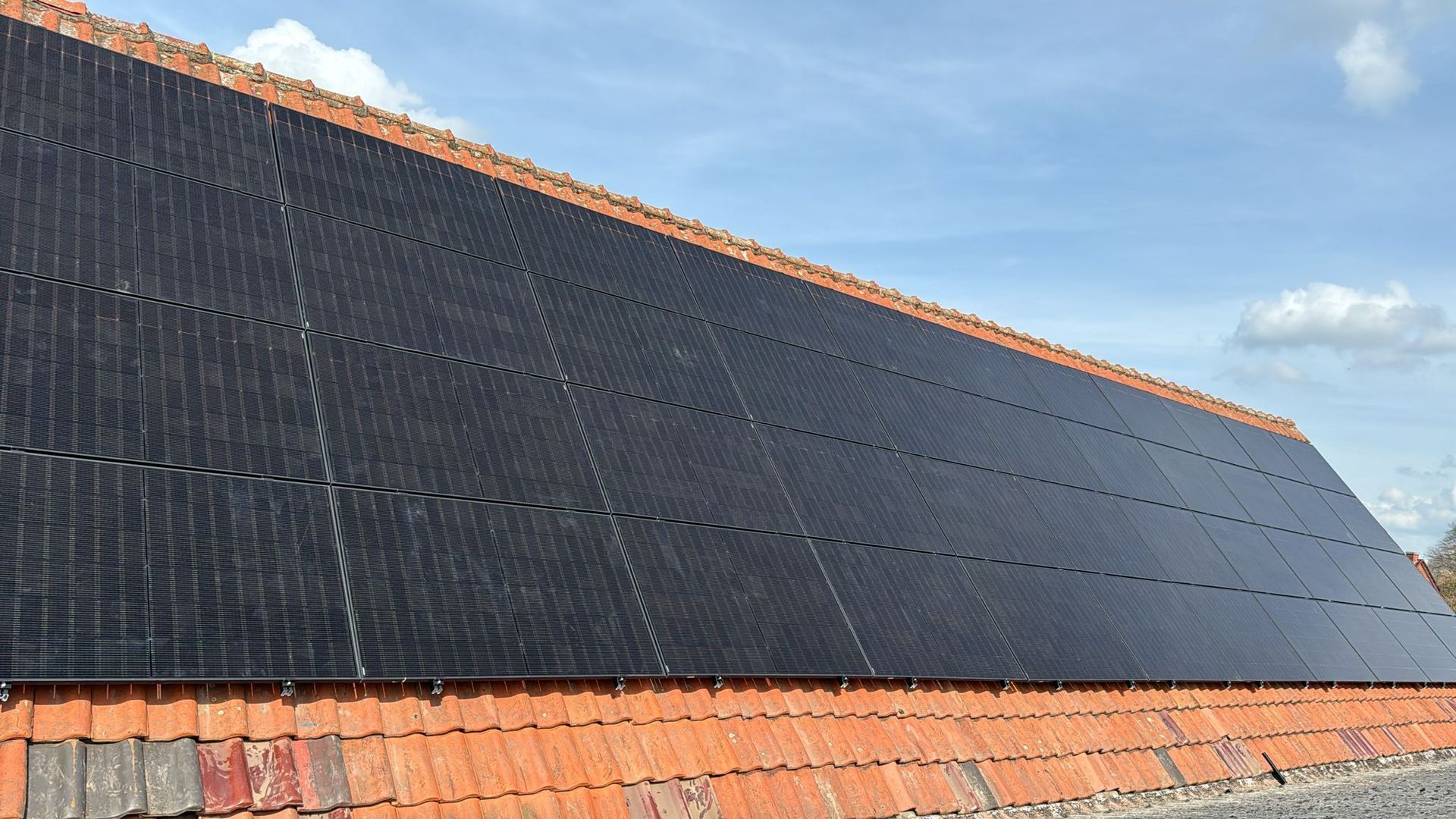Solarmodule auf einem roten Ziegeldach vor einem teilweise bewölkten blauen Himmel.