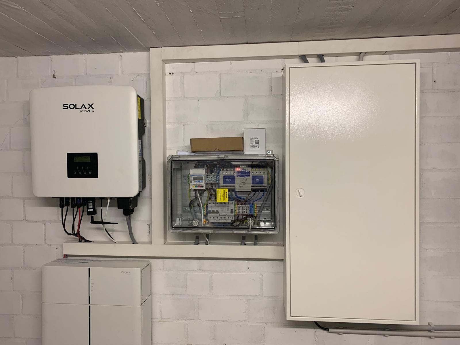 Solarpanel-Ausrüstung an einer Betonwand: ein Wechselrichter, ein Steuerkasten, ein großer Schrank und Batterieeinheiten.