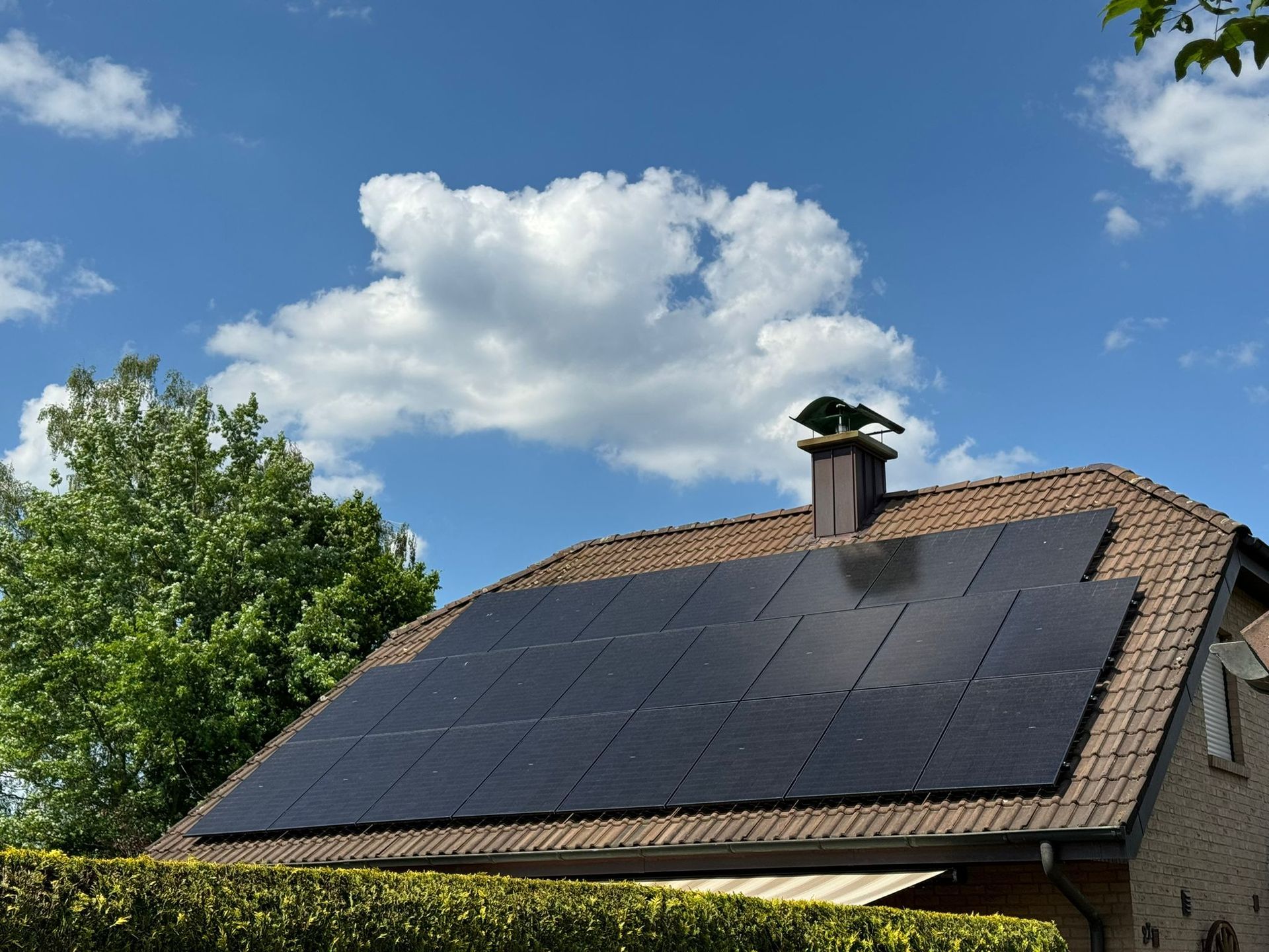Solarmodule auf einem braunen Ziegeldach vor einem teilweise bewölkten blauen Himmel.