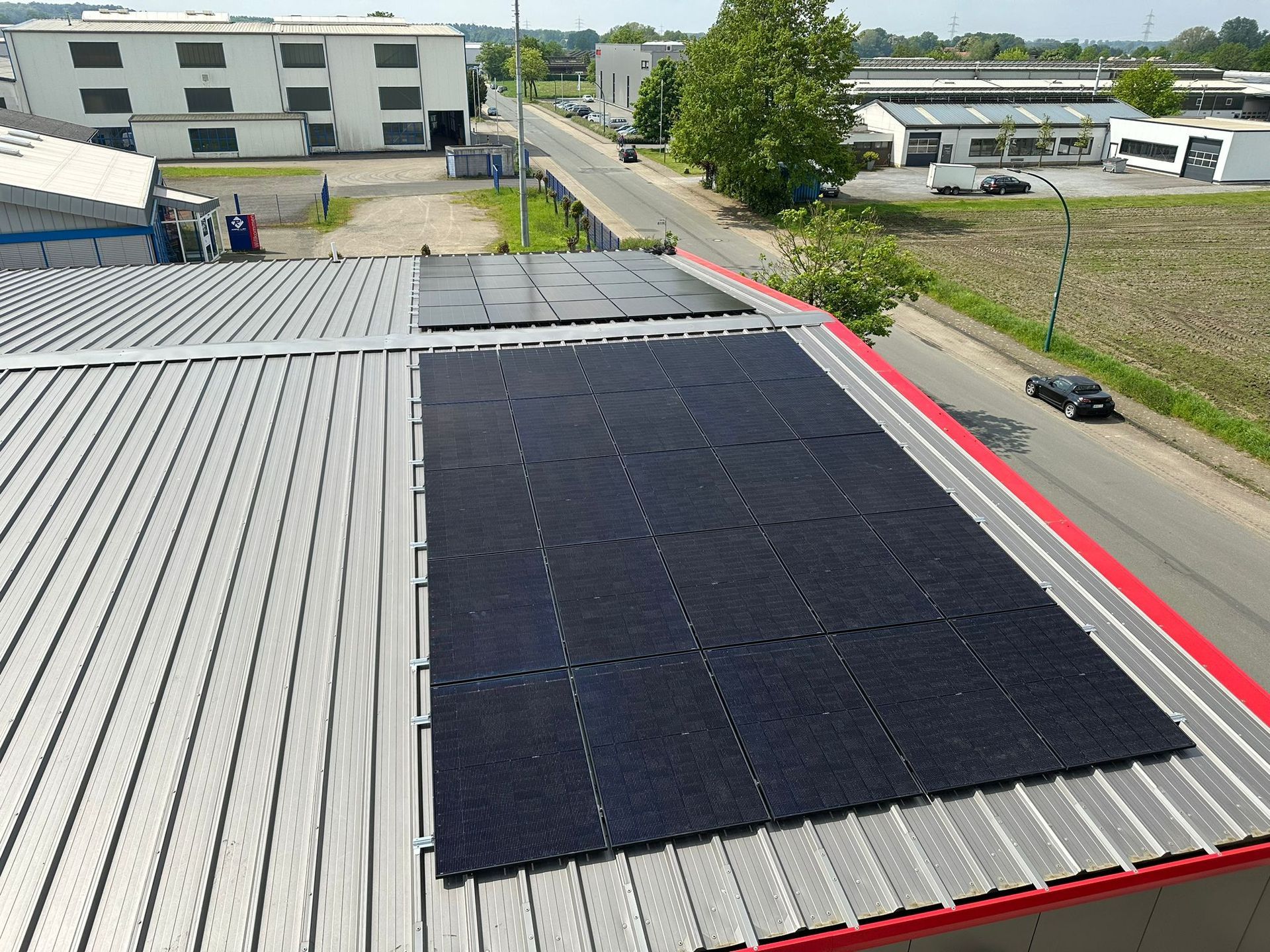 Auf einem Metalldach installierte Solarmodule in der Nähe einer Straße mit Autos und Gebäuden.