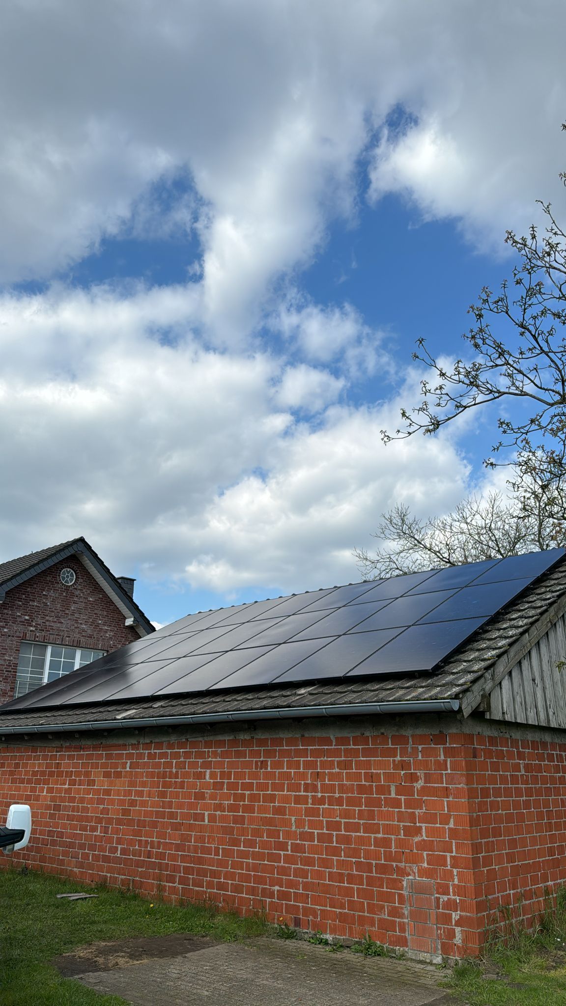 Sonnenkollektoren auf dem Dach eines Backsteingebäudes unter einem teilweise bewölkten blauen Himmel.