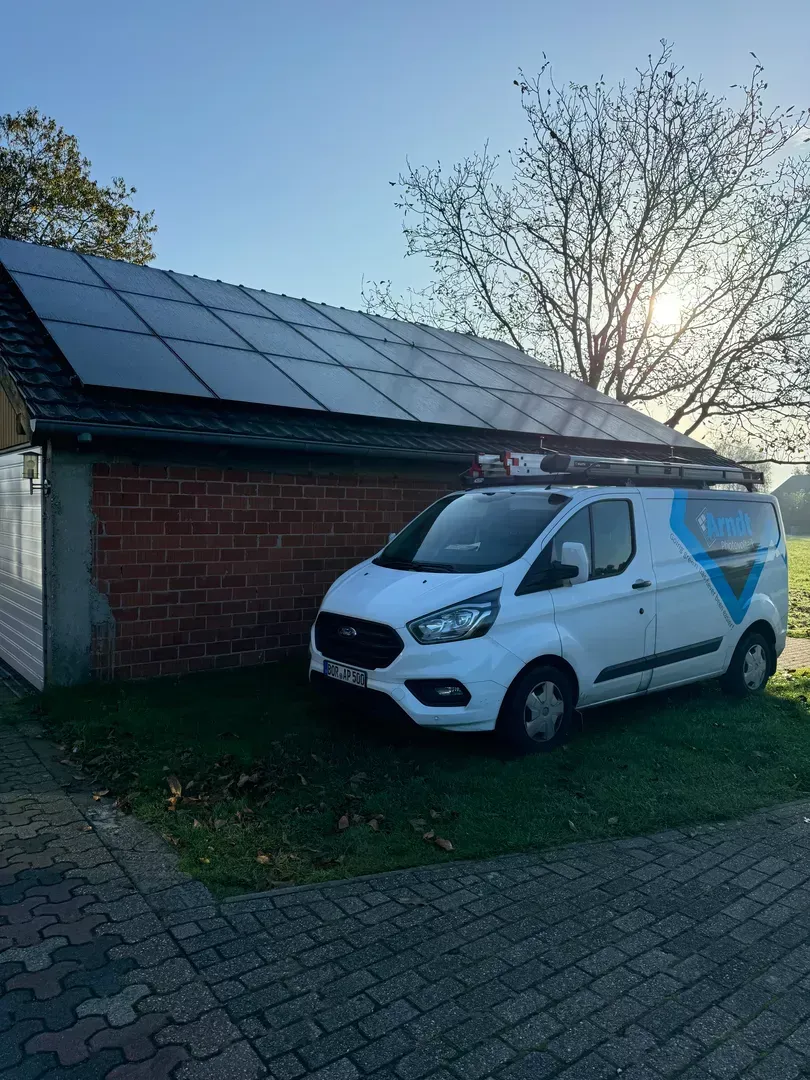 Weißer Service-Van parkt neben einem Backsteingebäude mit Solarzellen auf dem Dach. Die Sonne scheint.