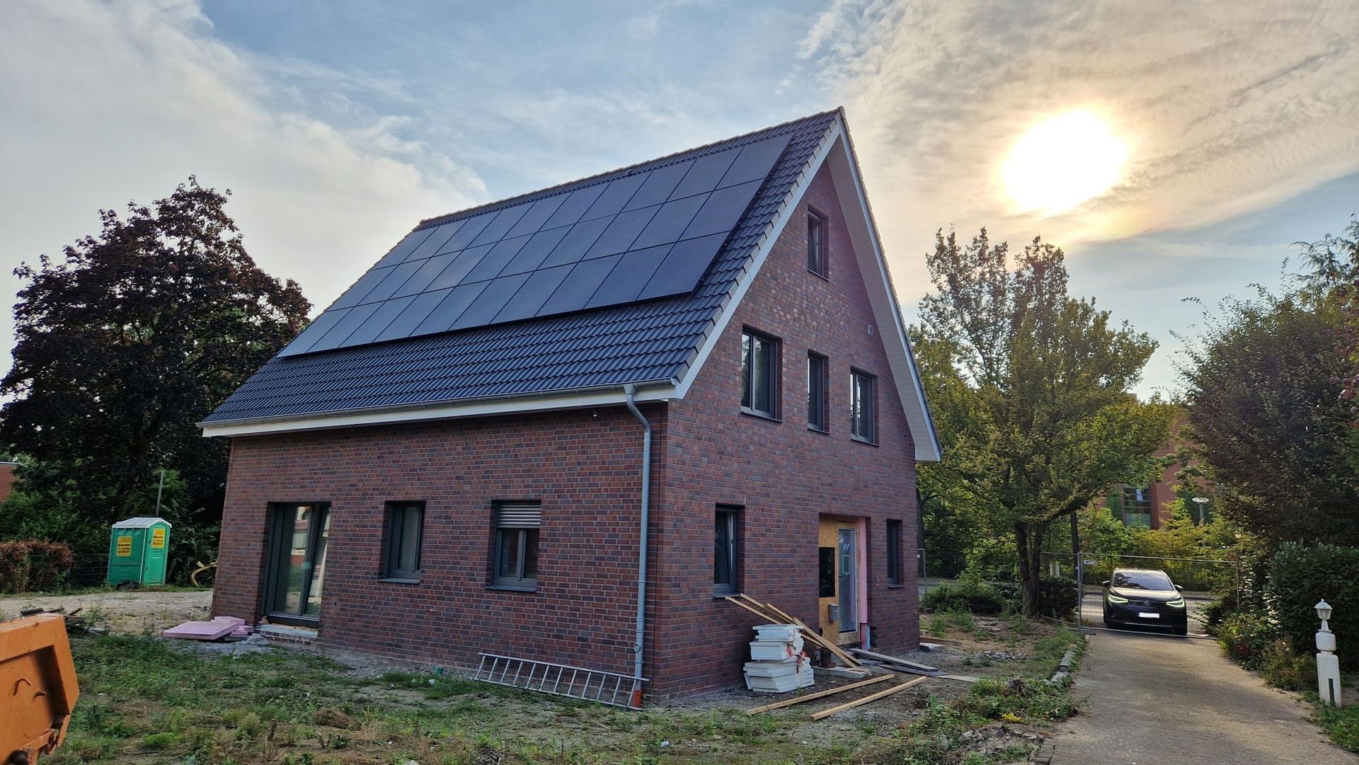 Backsteinhaus mit Solarzellen auf dem Dach, Sonnenlicht, Kiesauffahrt und einem LKW.