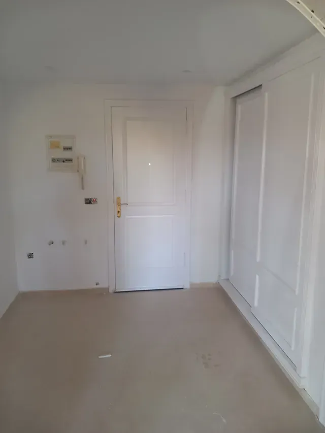 Una habitación vacía con paredes blancas y una puerta blanca.