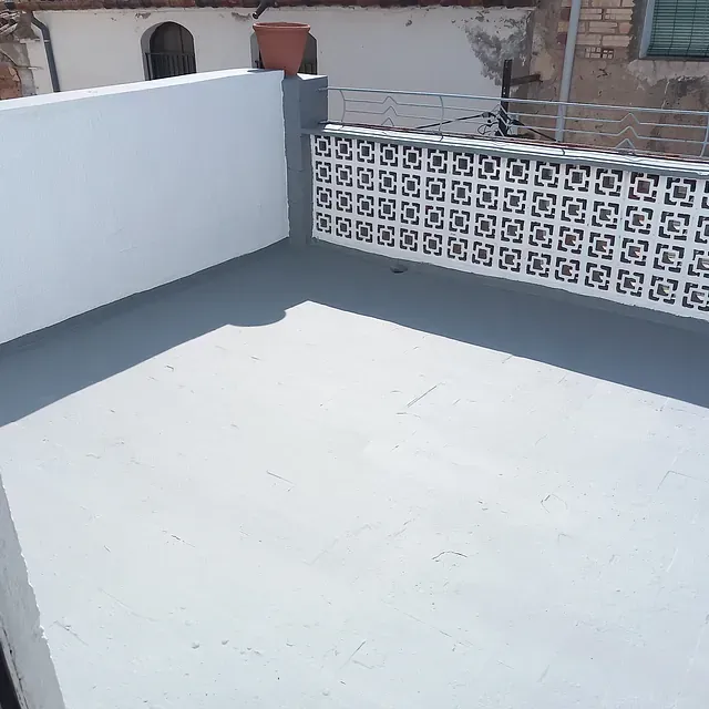 Un balcón con una pared blanca y un suelo gris.