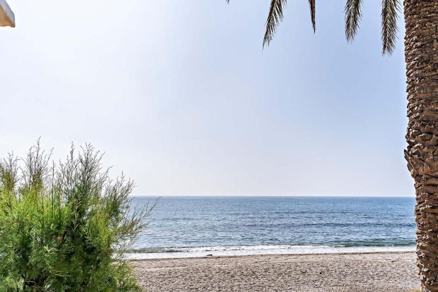 Playa de arena con ondulaciones, agua turquesa, cielo azul despejado y línea de árboles a lo lejos.