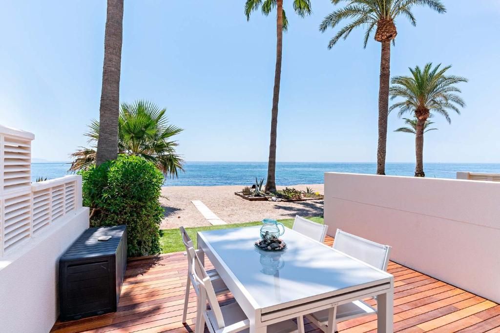 Comedor al aire libre con vistas a la playa. Mesa con sillas, vistas al mar, palmeras, cielo azul.