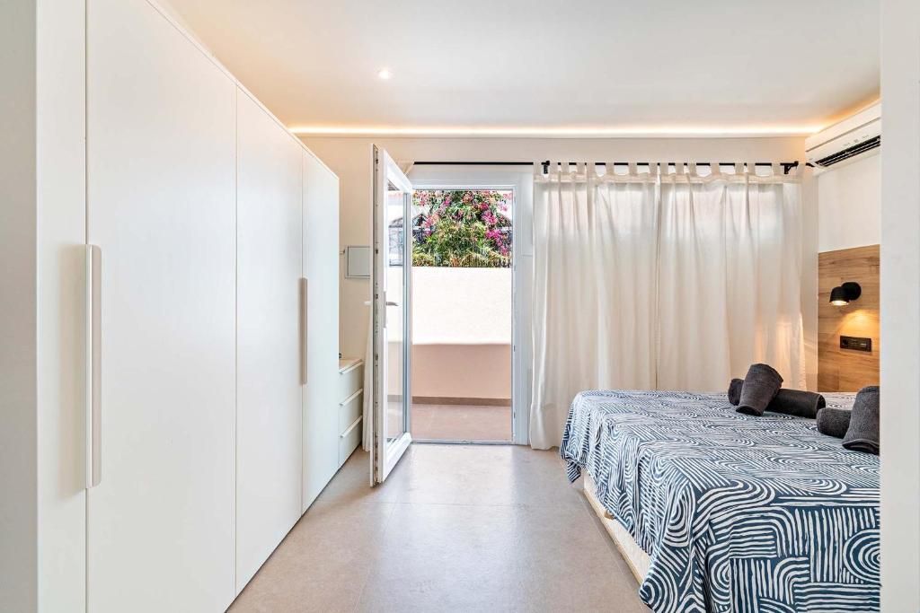 Dormitorio blanco con puerta de balcón abierta; cama con funda de estampado de cebra, armario blanco.