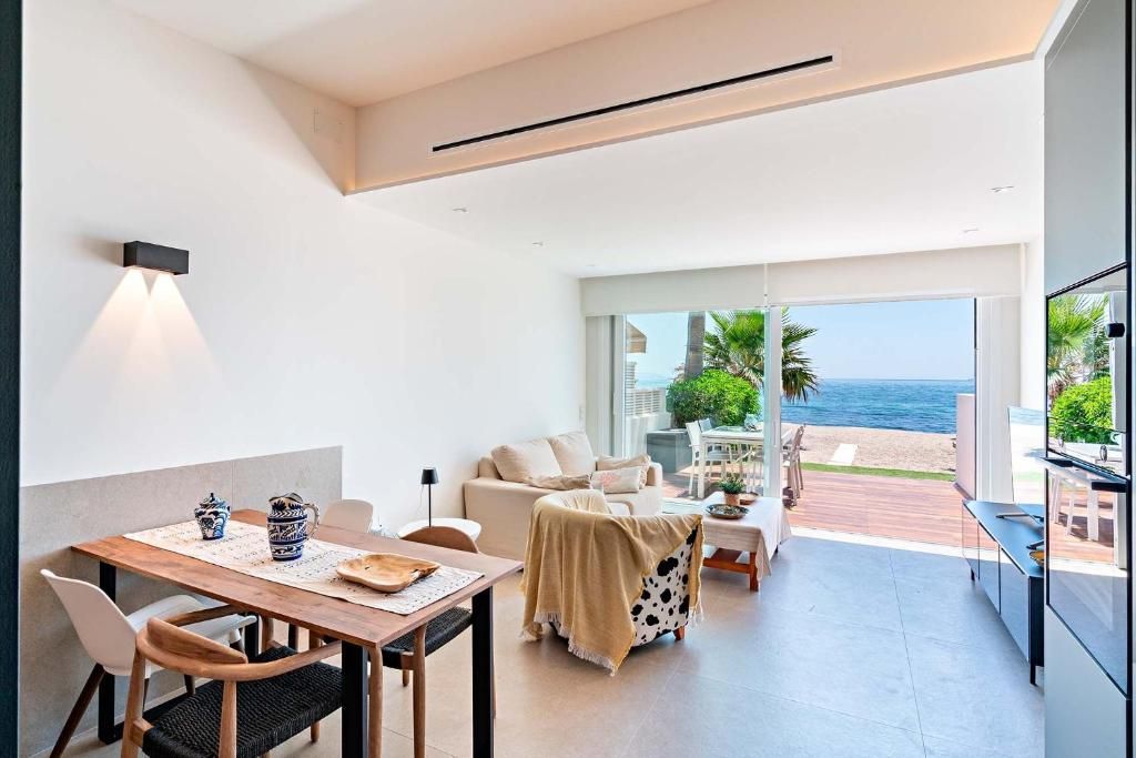 Espacio diáfano con comedor y zona de estar con vistas al océano a través de puertas correderas de cristal.