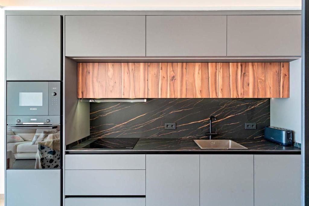 Cocina moderna con armarios grises, detalles en madera, encimera negra y horno empotrado.