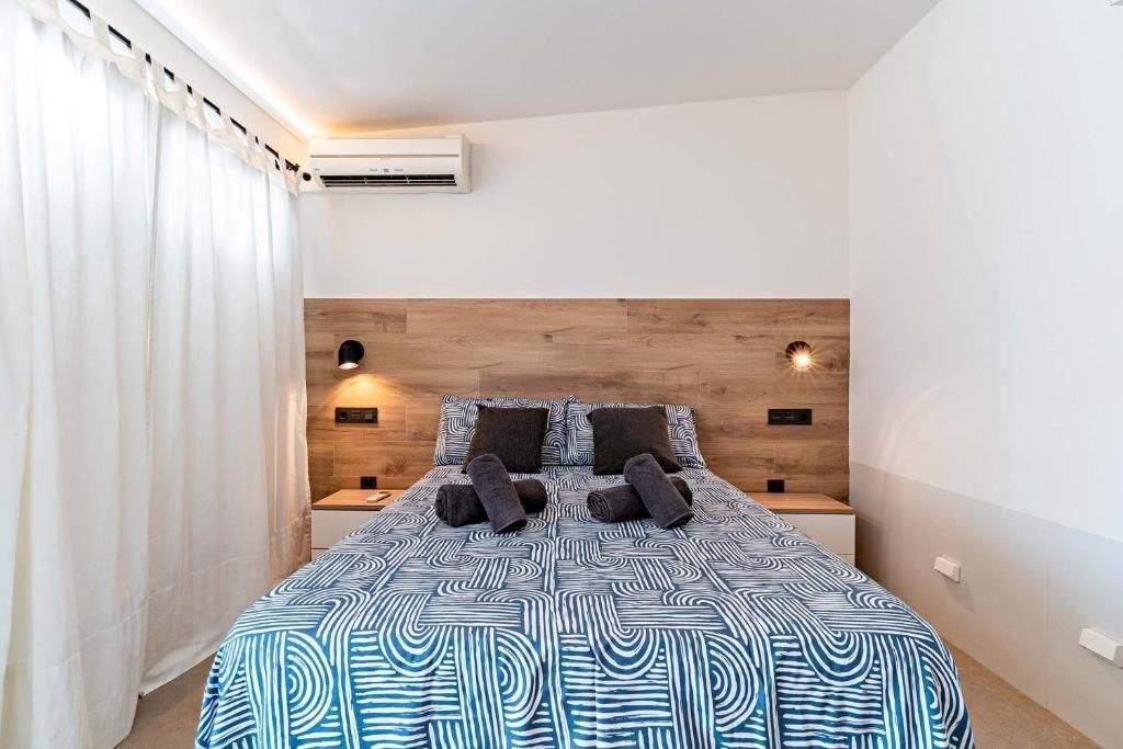 Dormitorio con cama, mesitas de noche y cabecero. Paredes blancas y cortinas traslúcidas.