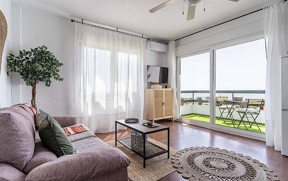 Acogedora sala de estar con sofá, mesa de centro y balcón con vistas a una luminosa zona exterior.