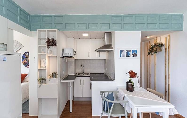 Pequeña cocina y comedor blancos con un toque turquesa, abiertos al dormitorio.