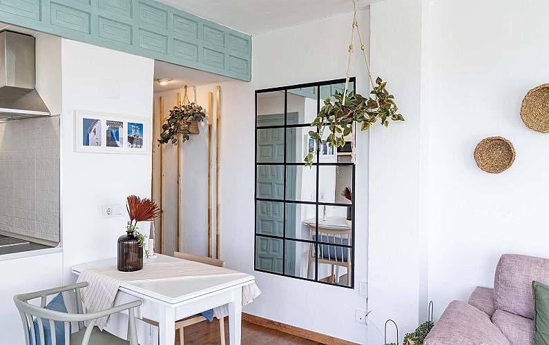 Acogedor comedor con una pequeña mesa blanca, un espejo con marco negro y un sofá rosa claro.