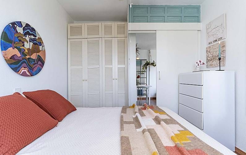 Dormitorio con cama, armario, cómoda, obras de arte y vista parcial a otra habitación.