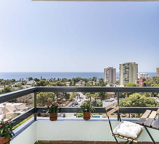 Comedor al aire libre con vistas a la playa. Mesa y sillas en una terraza de madera, palmeras y océano.