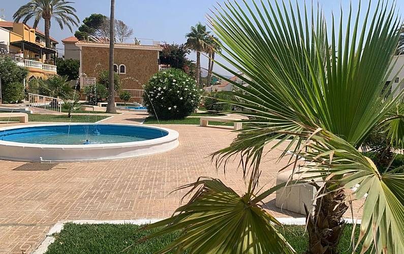 Patio con fuente, árboles y edificios. Palma en primer plano. Colores azul, marrón y verde.