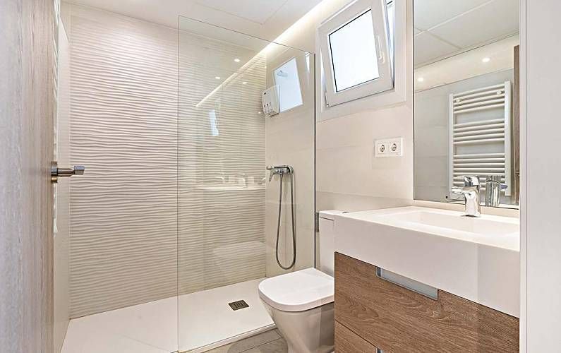 Baño moderno con ducha a ras de suelo, inodoro blanco, lavabo y azulejos texturizados en las paredes.