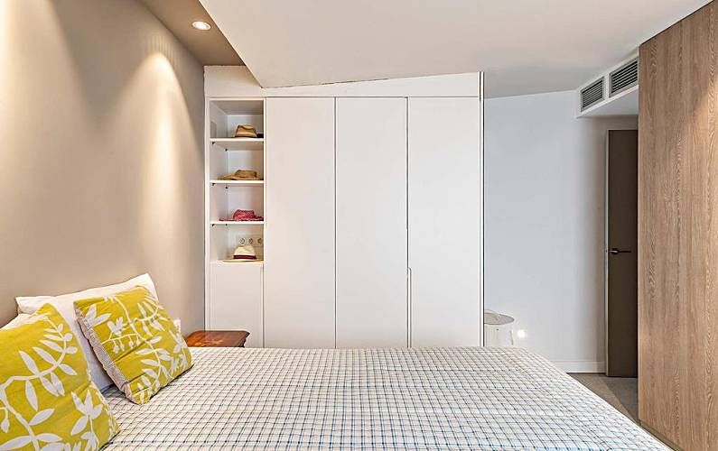Dormitorio con armario blanco, estanterías empotradas, cama con almohadas amarillas y puerta de madera.
