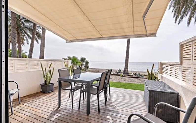 Patio con mesa y sillas con vistas a la playa y al océano bajo un toldo retráctil.
