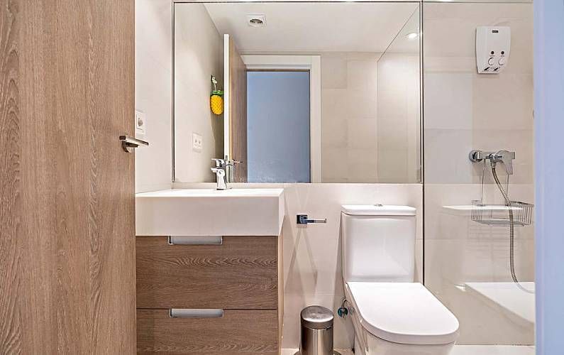 Baño pequeño y moderno con tonos blancos y madera. Lavabo con espejo, inodoro y grifería de ducha.
