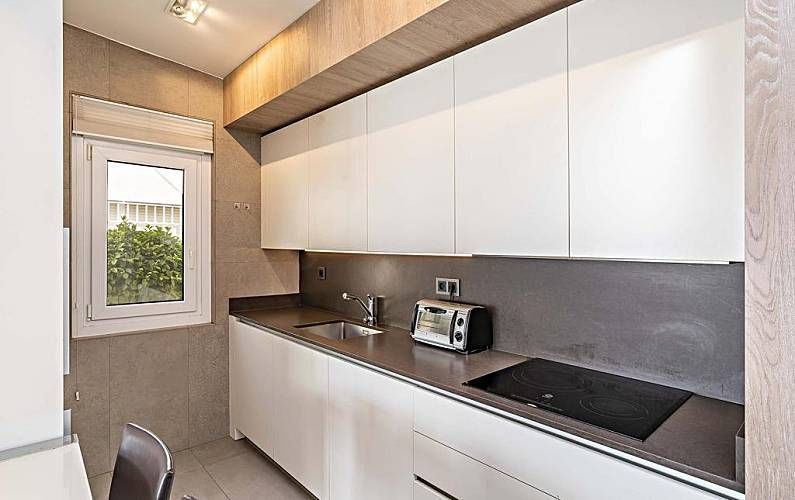 Cocina moderna con armarios blancos, encimera de acero inoxidable y ventana pequeña.