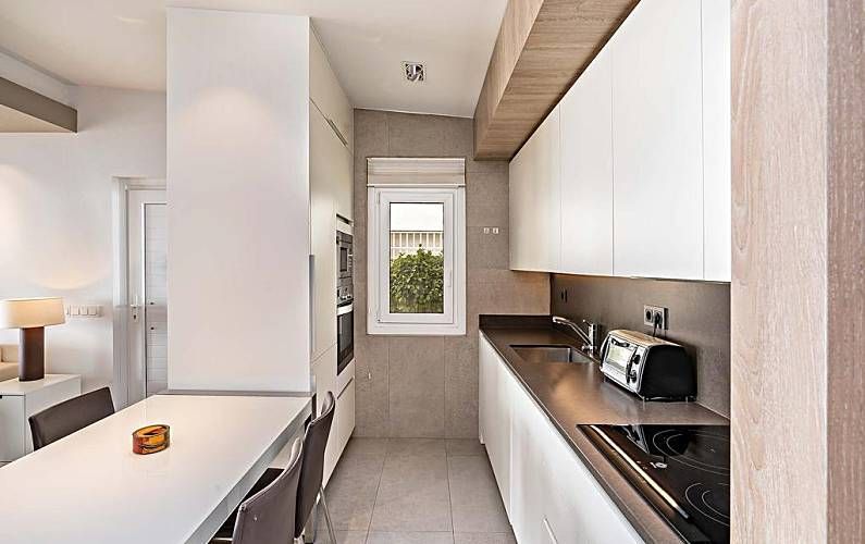 Cocina moderna y estrecha con armarios blancos, encimera de acero inoxidable y una pequeña ventana.