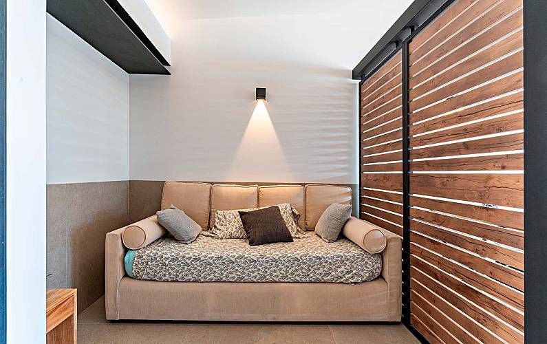 Acogedora zona de estar con sofá color beige, cojines decorativos, puerta corredera de madera y aplique de pared.