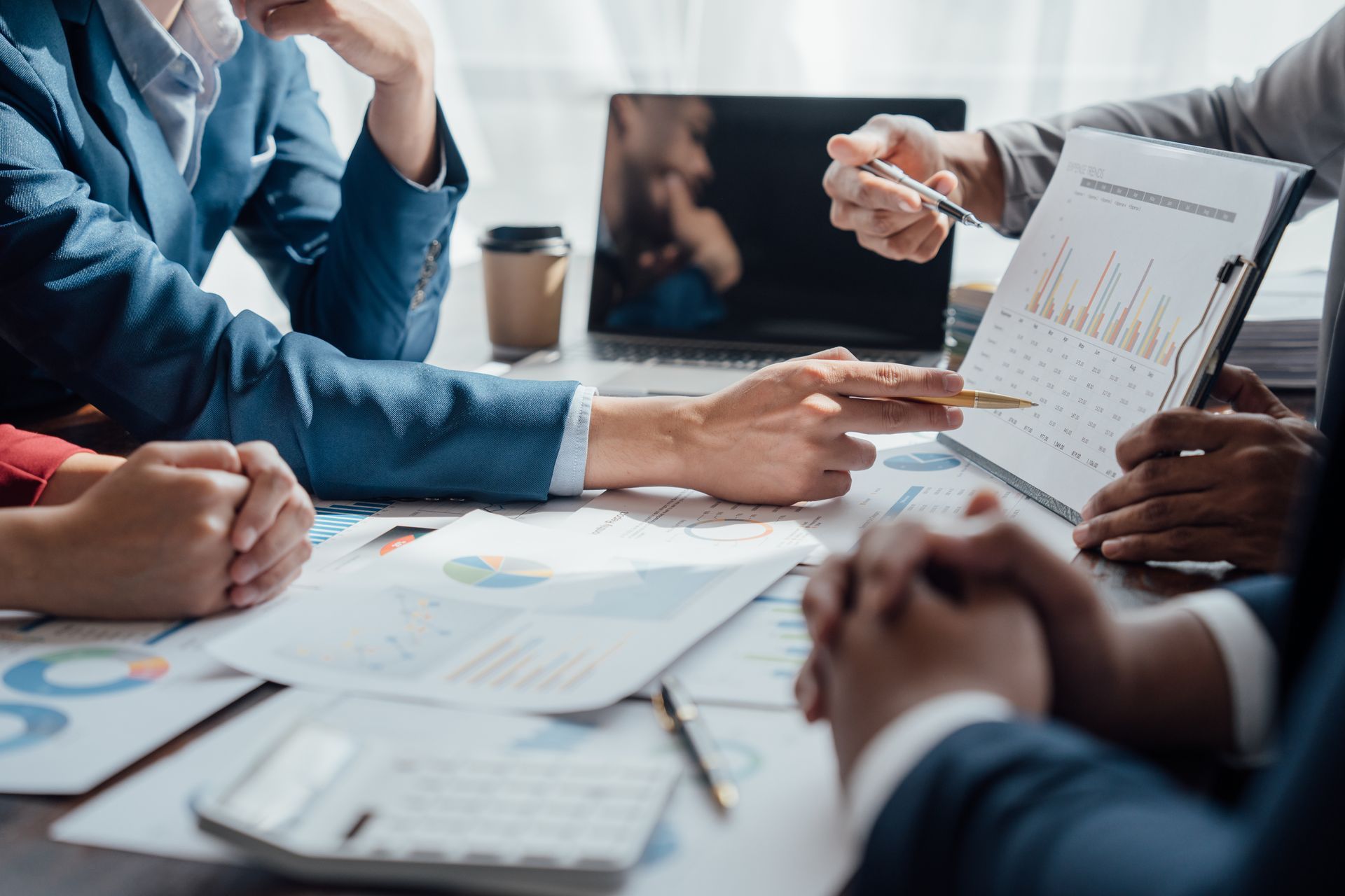 Eine Gruppe von Leuten sitzt mit Papieren und einem Laptop um einen Tisch herum.
