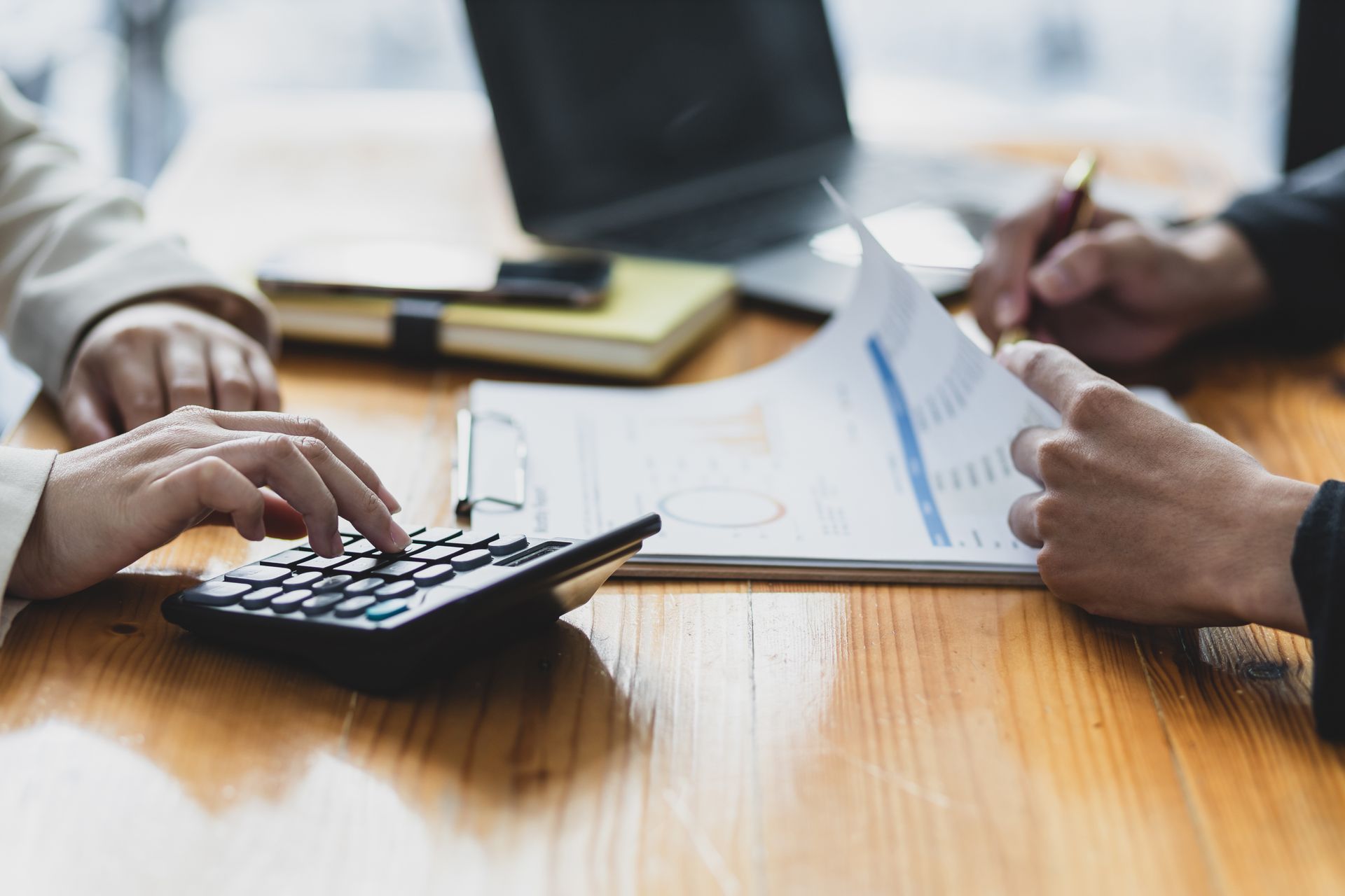 Eine Person benutzt einen Taschenrechner, während eine andere Person auf ein Blatt Papier schreibt.